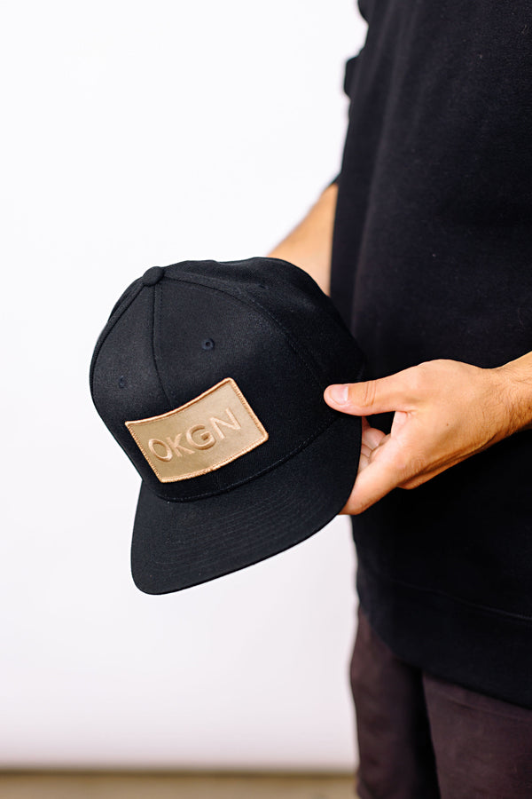 Our abbreviated OKGN logo, tan on tan stitched onto our favorite black snapback