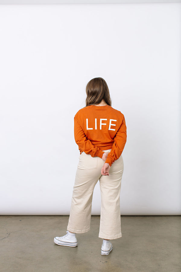 Okanagan Lifestyle orange long sleeve shirt with LIFE printed in white on back.