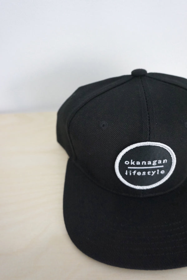 The Classic Okanagan Lifestyle wordmark logo embroidered white on our favorite youth size black snapback